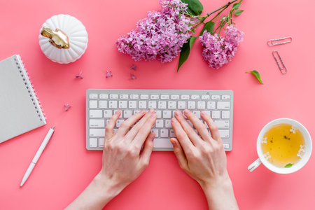 Girl typing on computer keyboard bright office space with flowers. Above view