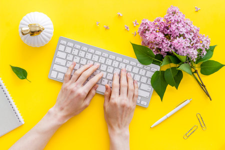 Girl typing on computer keyboard bright office space with flowers. Above view