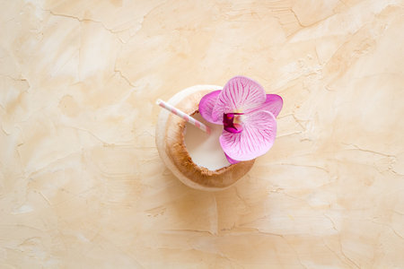 Raw coconut water or milk with straw and orchid flower, above view
