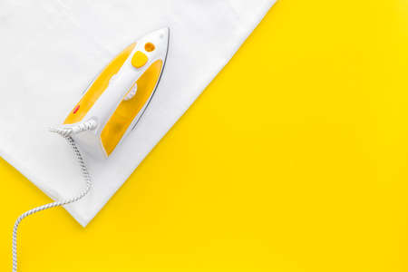 Yellow iron with clean linen on ironing board. Top view, copy spaceの写真素材