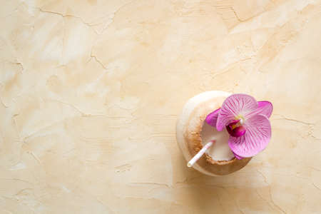 Coconut drink with straw on beach, top view copy space