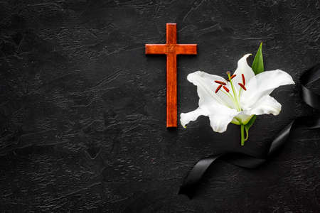 Funeral lily flowers with cross on dark stone background. Mourning symbolsの写真素材