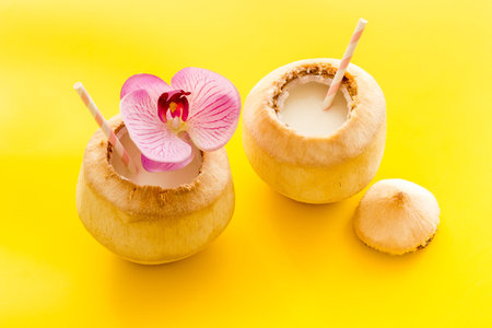 Raw coconut water or milk with straw and orchid flower, above view