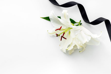Flat lay of lily flowers and black ribbon. Funeral symbol