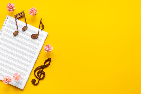 Musical sheet with wooden notes and flowers, top view