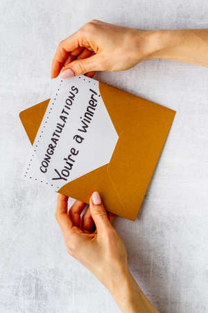 Hands holding award congratulation card in golden envelope. Text Youre a winner in letterの写真素材