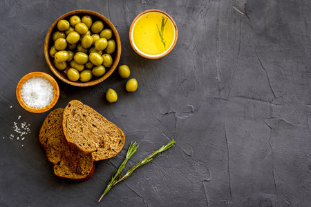 Olives in wooden bowls with sliced bread and oil, top view