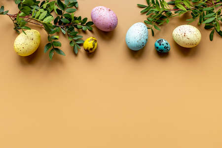 Layout of colorful Easter eggs with spring branches and green leaves, top view