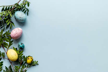 Layout of colorful Easter eggs with spring branches and green leaves, top view