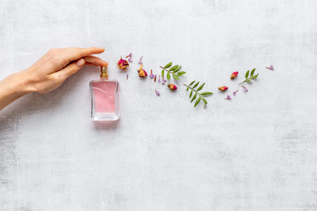 Female hand spray perfume bottle and flow of flowers