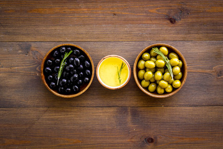 Olives in wooden bowl with oil and rosemary leaves, top viewの写真素材