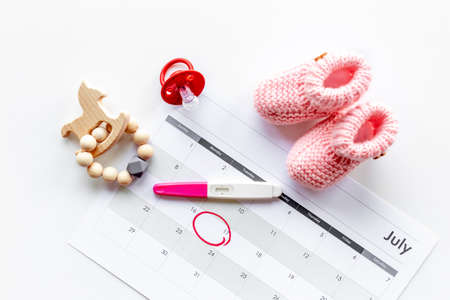 Pink baby girl booties with pregnancy test on calendar, top viewの写真素材