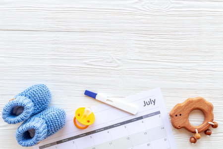 Pregnancy test with blue baby boy booties and calendar, top view