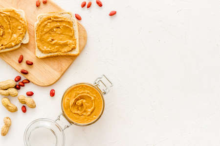 Glass jar of peanut butter with sandwiches and nuts on kitchen tableの写真素材