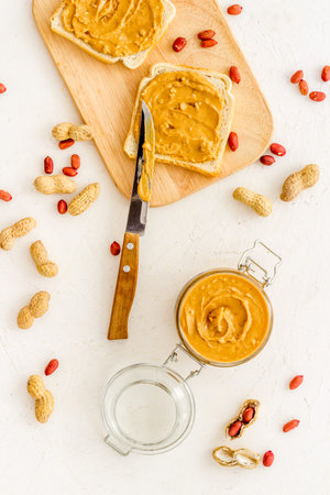 Glass jar of peanut butter with sandwiches and nuts on kitchen table