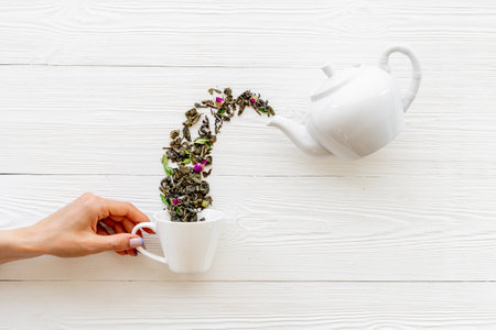 Female hand pours tea leaves from teapot in cupの写真素材