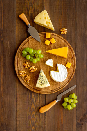 Set of cheese on wooden board with cheese knives, top view