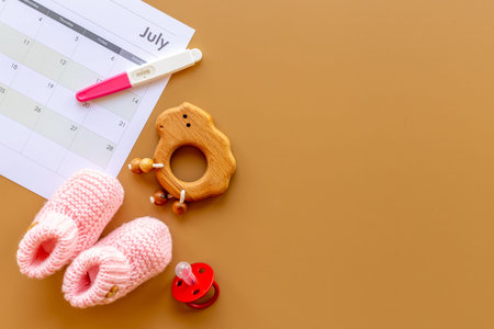Pregnancy test with pink baby girl booties and calendar, top view