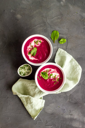 Two white bowls of red beet soup with sour cream and green herbal salt