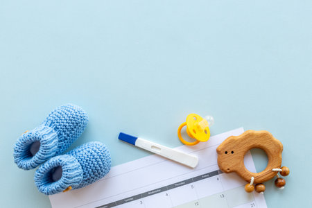 Blue baby boy booties with pregnancy test on calendar, top view