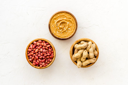 Creamy peanut butter and nuts in wooden bowls, top view