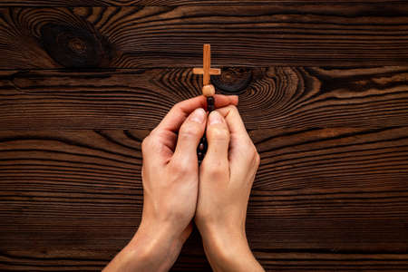 Sending prayer to god - rosary in hands with wooden crossの写真素材
