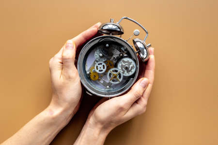 Hands holding alarm clock mechanism with steel gears and wheels close upの写真素材