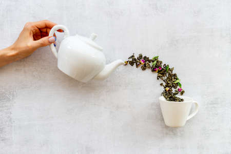 Female hand pours tea leaves from teapot in cup