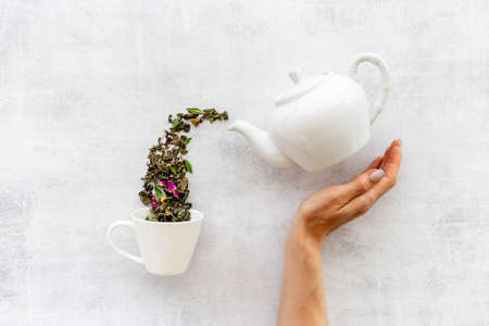 Female hand pours tea leaves from teapot in cupの写真素材