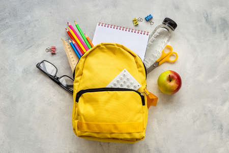 Back to school concept. Yellow school backpack with supplies water and appleの写真素材