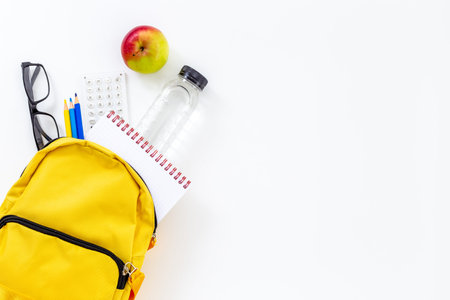 Back to school concept. Yellow school backpack with supplies water and apple