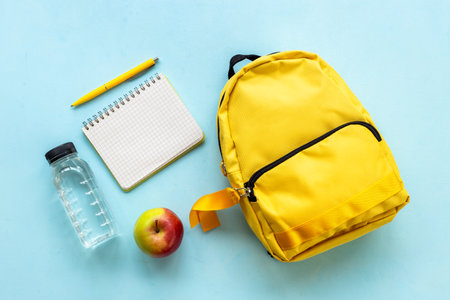 Back to school concept. Yellow school backpack with supplies water and appleの写真素材