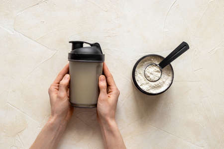 Sport shaker bottle in hands and whey protein in jar. Fitness and gym diet nutritionの写真素材