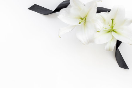 Flowers heads of white lilies with black ribbon. Mourning or funeral backgroundの写真素材