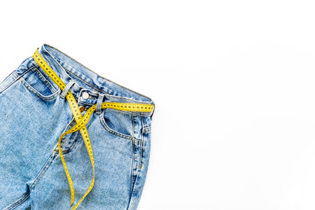 Weight loss concept. Jeans with yellow measuring tape instead of a beltの写真素材