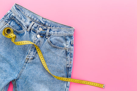 Weight loss concept. Jeans with yellow measuring tape instead of a beltの写真素材