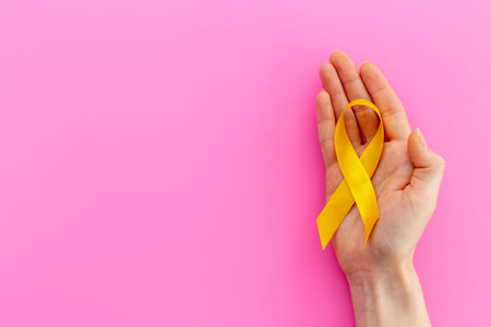 Yellow ribbon symbol of bone cancer with hands. Medical support and prevention.の写真素材