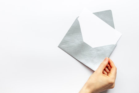 Hand holds blank paper against envelope for letters. Space for text, top view.の写真素材