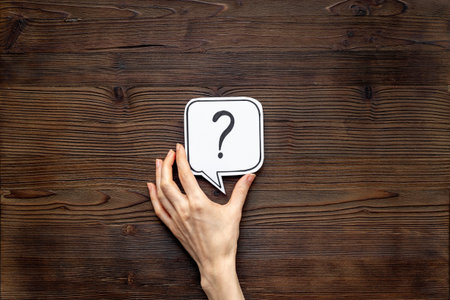 Hand holding question mark on paper speech bubble, top view