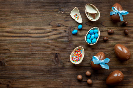 Chocolate Easter eggs in blue ribbon with sweets on brown wooden background.