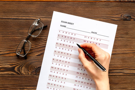 Female hand with answer exam sheet form on a table, top view. Education background.