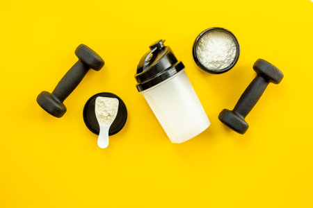 Protein powder in jar and scoop for sports nutrition with black dumbbells, top view.の写真素材