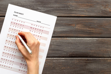 Female hand with answer exam sheet form on a table, top view. Education background.