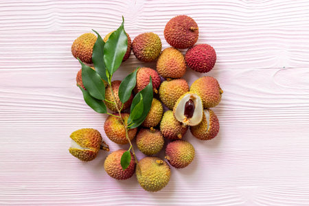 Juicy lychee fruit with cut in half and green leaves, top view. Fresh ripe tropical fruit.