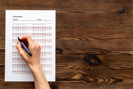 Female hand with answer exam sheet form on a table, top view. Education background.の写真素材
