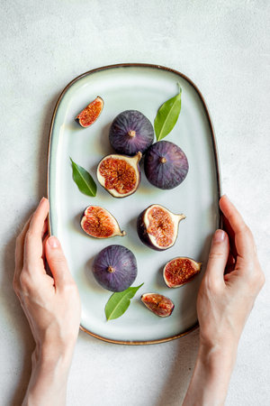 Female hands are holding plate with ripe figs whole and cut. Top view.の写真素材
