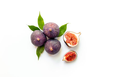 Fresh ripe figs whole and cut with green leaves on white background. Top view.
