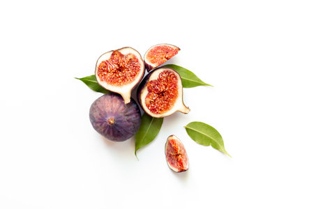 Fresh ripe figs whole and cut with green leaves on white background. Top view.の写真素材