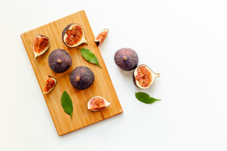 Plate with fresh ripe figs whole and slices with green leaves on wooden cutting board. Top view.