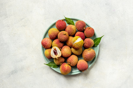 Juicy fresh lychee fruit with cut in half and green leaves on the plate, top view.の写真素材